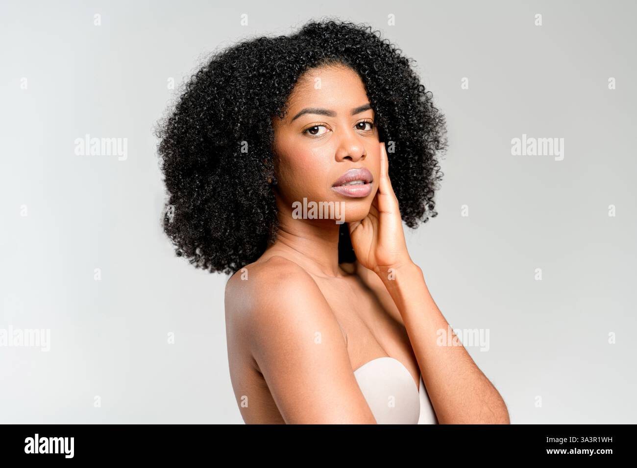 Eine introspektive afroamerikanische Frau hat eine nachdenkliche Pose, ihr Blick leicht abgewendet, vor einem klaren Hintergrund, der ihre reflektierende Stimmung betont. Stockfoto