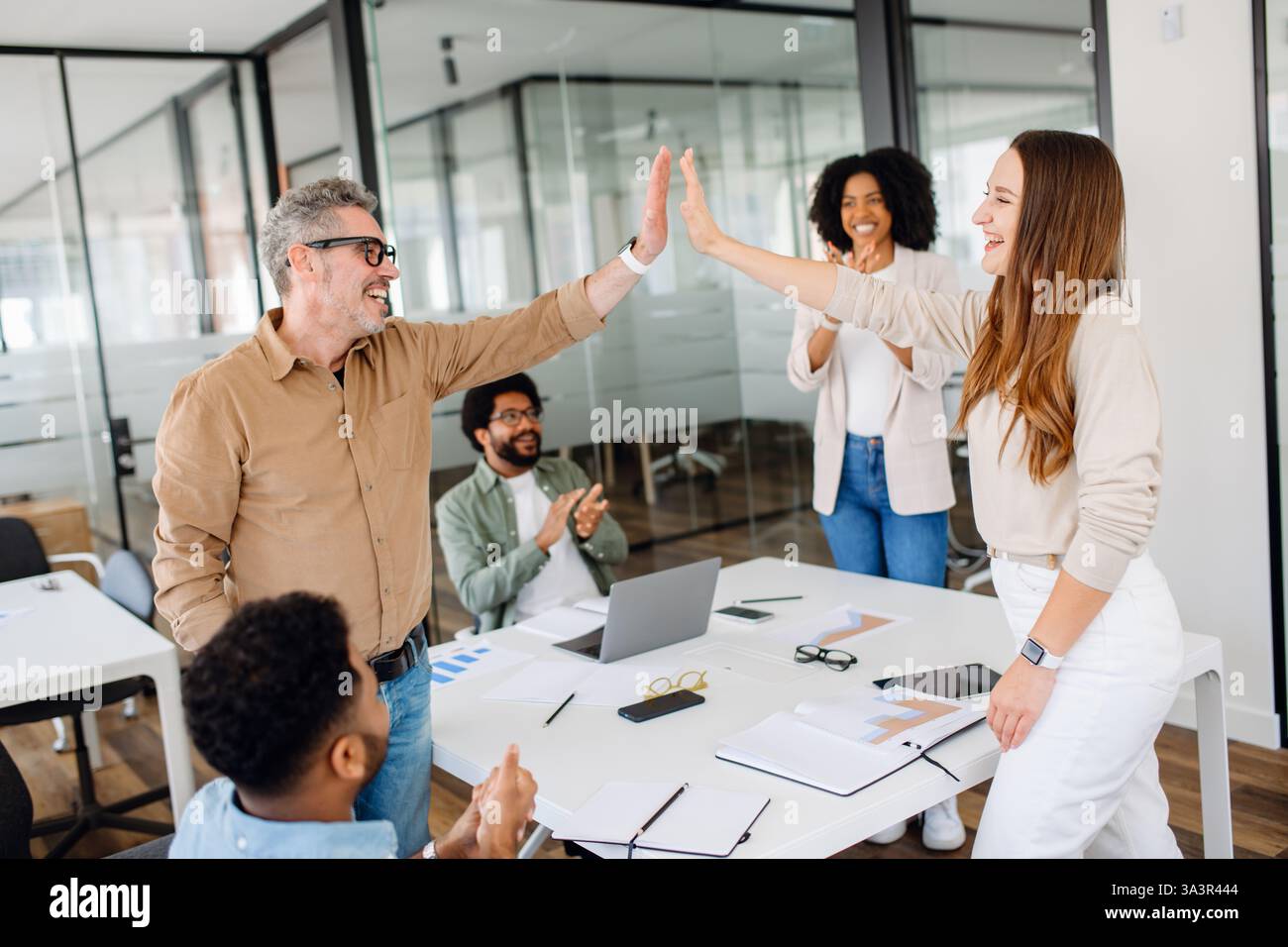 Glückliche Kollegen feiern eine Leistung in einer lebendigen Büroumgebung. High Fives und Applaus schaffen eine dynamische Atmosphäre aus Unterstützung, Teamarbeit und beruflicher Motivation. Stockfoto