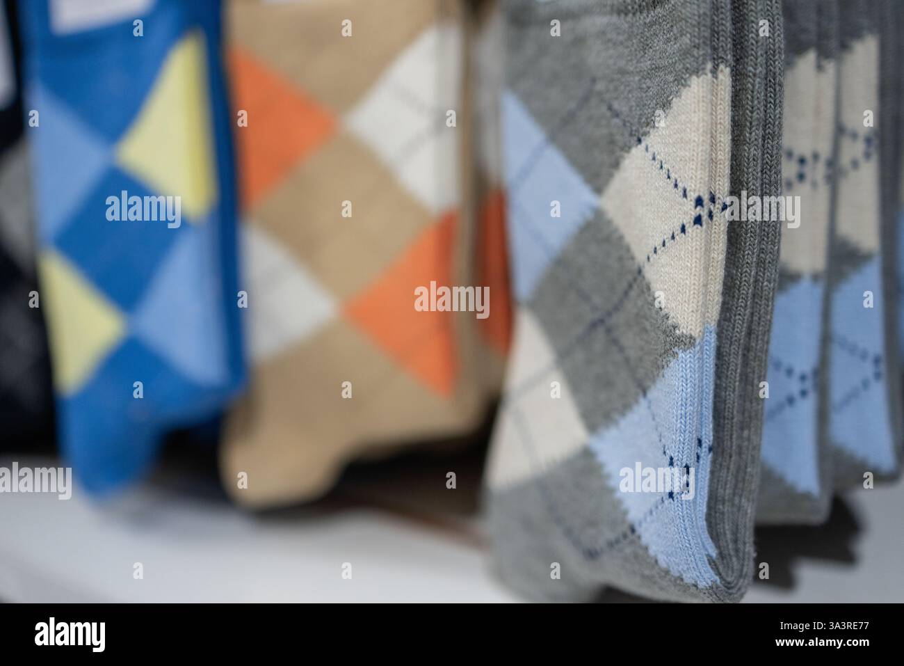 Ein Stapel gemusterter Socken mit klassischem Argyle-Design in mehreren Farben, die gleichmäßig auf einem Einzelhandelsdisplay gefaltet sind und die Textur und Geom hervorheben Stockfoto