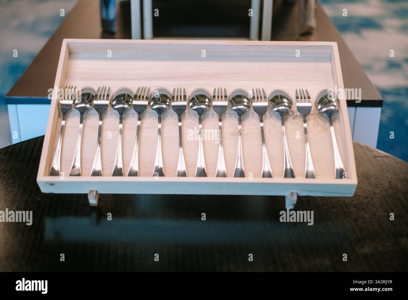 Ordentlich angeordnete silberne Gabeln und Löffel in einem hellen Holztablett. Das reflektierende Metallbesteck verleiht einen Hauch von Raffinesse. Perfekt für Catering, Re Stockfoto