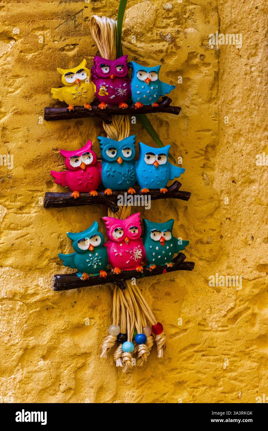 Farbenfrohe Dekorative Eulenfiguren hängen an einer gelb strukturierten Wand Stockfoto