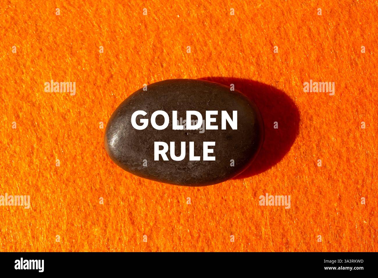 Goldene Regelbotschaft auf schwarzem Stein auf orangem Hintergrund. Konzeptionelles goldenes Regelsymbol. Kopierbereich. Stockfoto