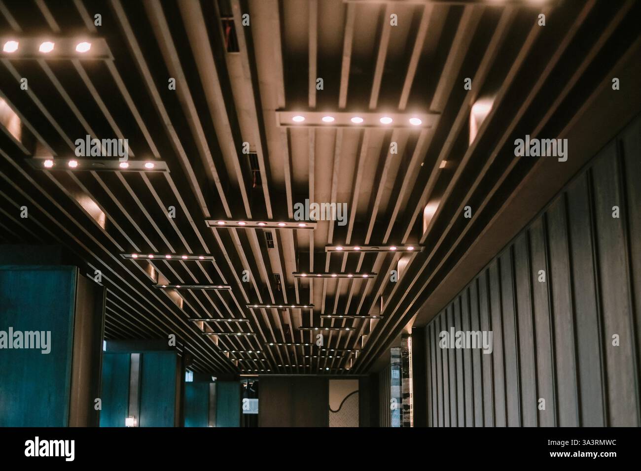 Eine moderne architektonische Decke mit parallelen Holzbalken und Einbauleuchten. Das Design sorgt für ein stilvolles und rhythmisches Muster, das eine zusätzliche Note verleiht Stockfoto