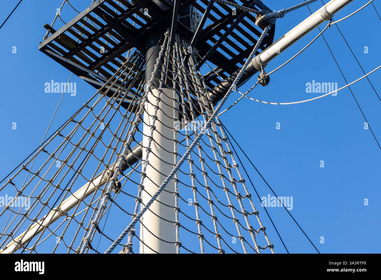 Blick auf einen Schiffsmast, eine Plattform und ein Seil mit traditionellen maritimen Details vor einer lebendigen Kulisse mit blauem Himmel Stockfoto