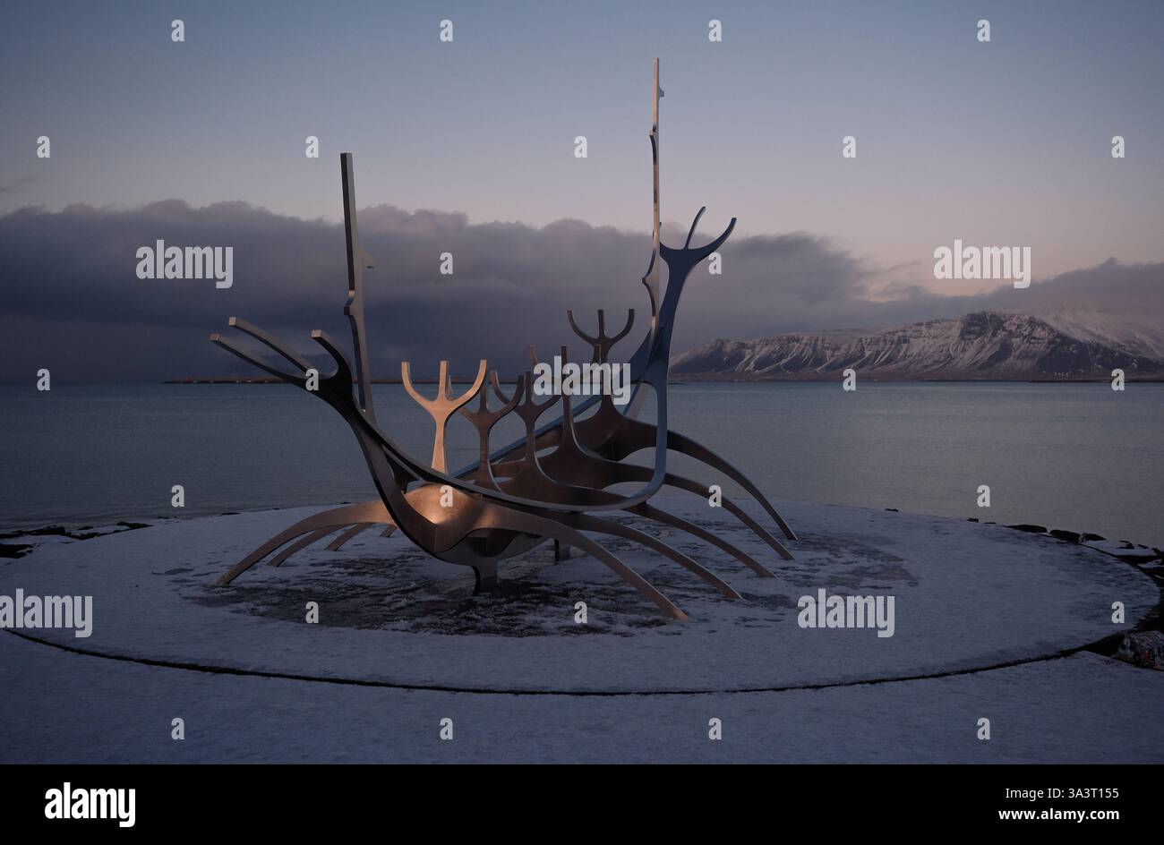 Das Sun Voyager Art Wahrzeichen in Reykjavik Island fängt die Abendsonne vor einer dunklen stürmischen Kulisse mit dem Mount Esja im sanften Licht der Sonne ein Stockfoto
