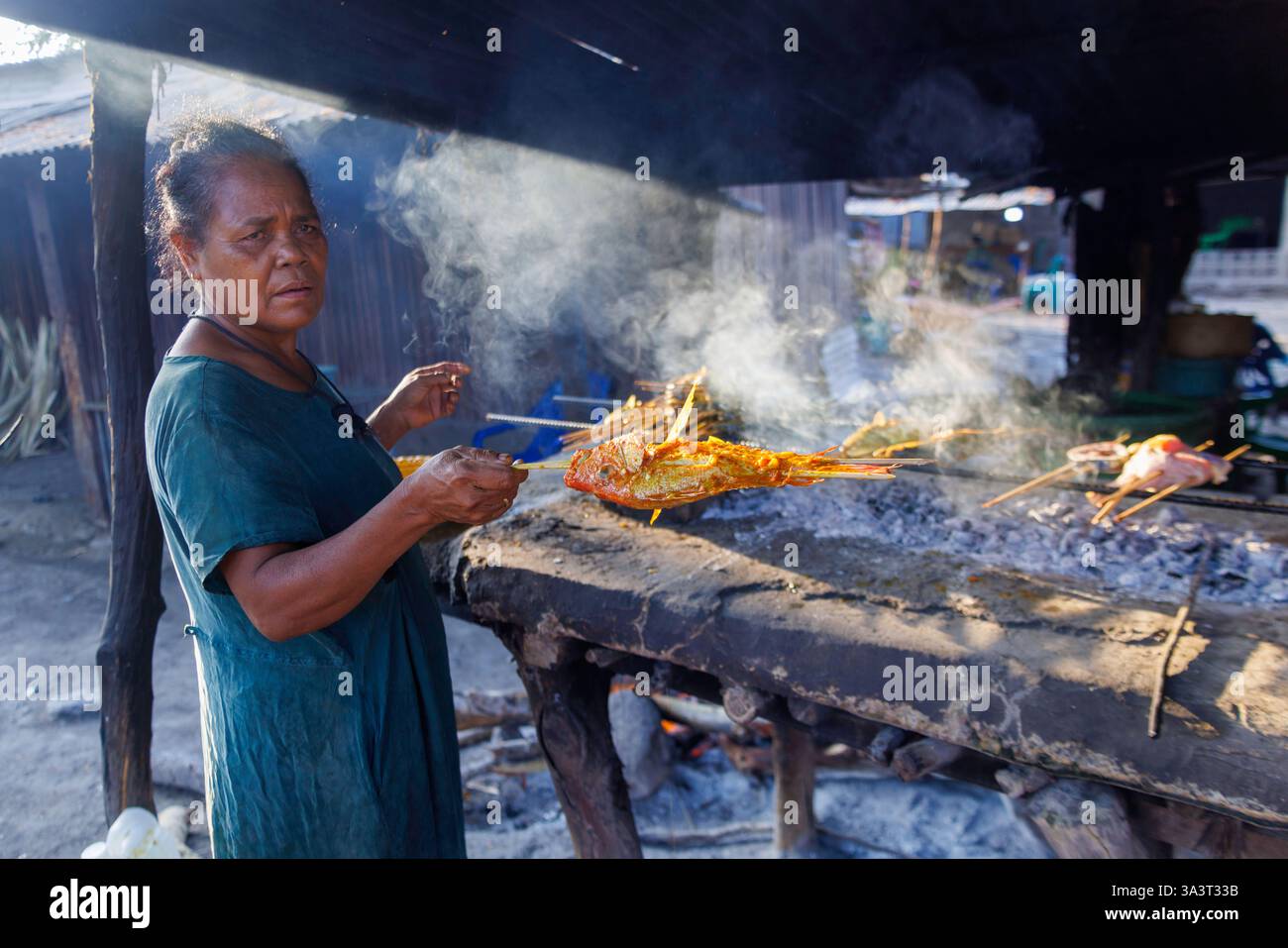 Eine Frau, die Fisch auf einem offenen Feuer auf einem Straßenmarkt in der Nähe von Baucau in der Demokratischen Republik Timor-Leste kocht. Stockfoto