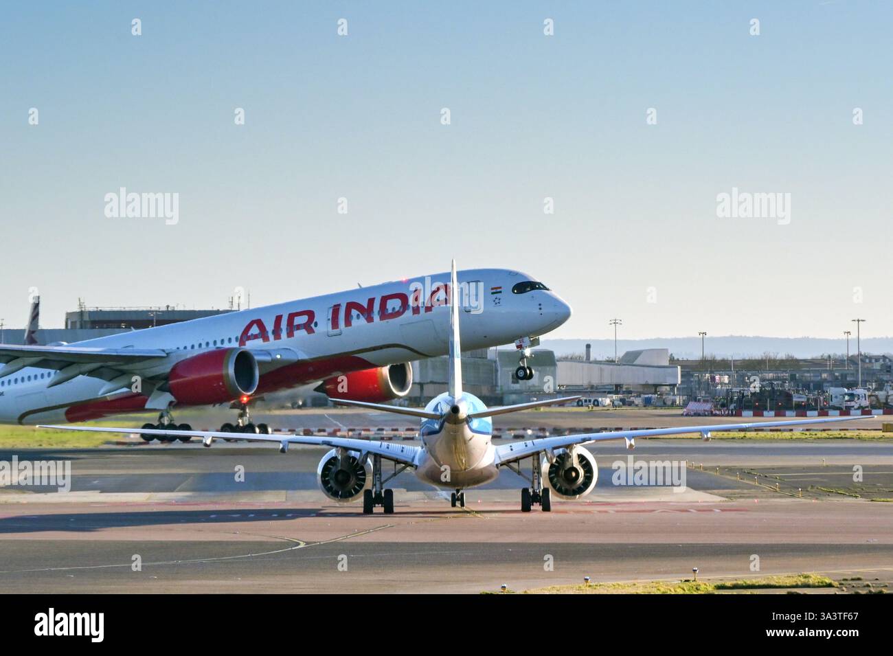 London, England, UK - 3. Januar 2025: Ein kleiner Jet wartet auf die Überquerung einer Landebahn am Flughafen London Heathrow, während ein Air India Airbus A350 startet Stockfoto