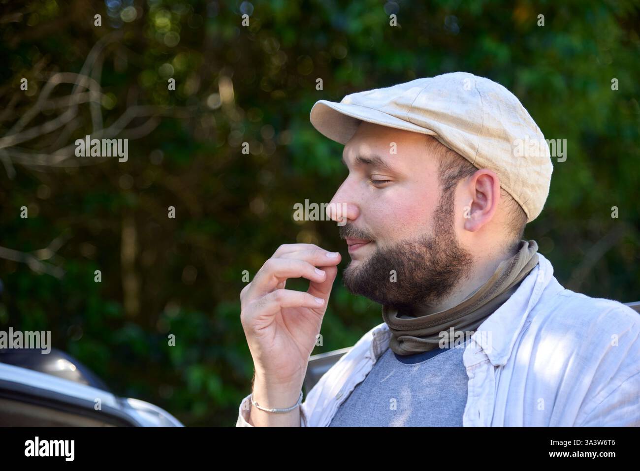 Porträt eines jungen Mannes im Freien, der etwas Unerkennbares genießt, das er isst. Sein Lächeln und sein Ausdruck vermitteln Wohlbefinden und positive Gefühle Stockfoto