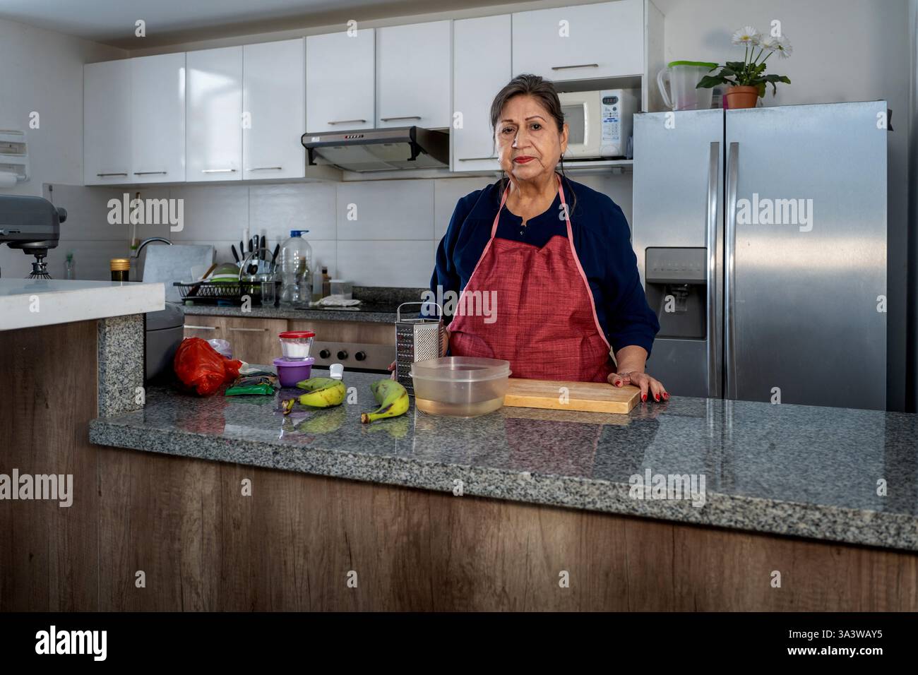 Ältere hispanische Frau, die Schürze trägt, in der Küche steht und Zutaten für das Kochen vorbereitet Stockfoto