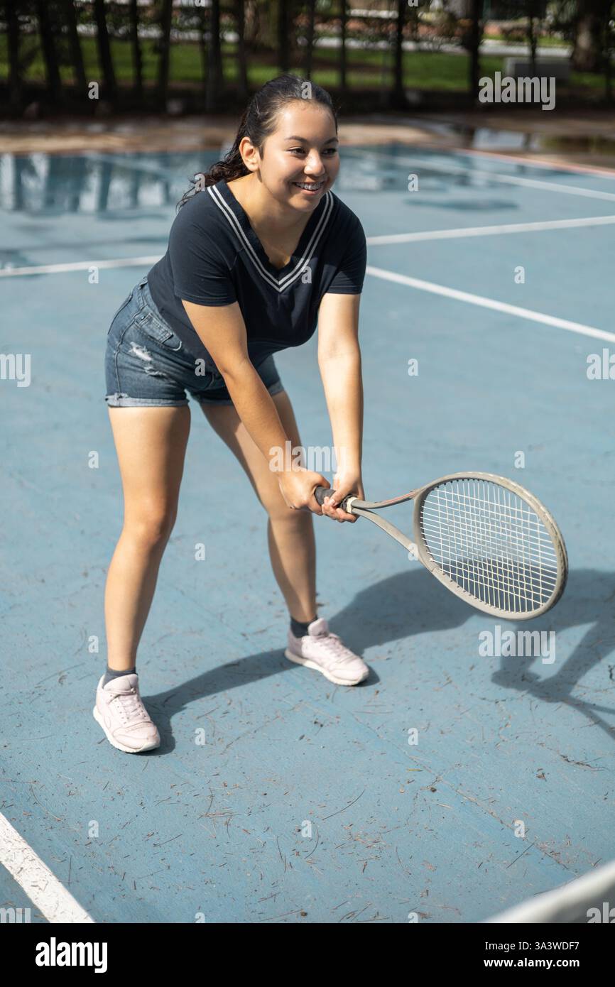 Ein hübsches Mädchen in Shorts spielt Tennis und hält selbstbewusst ihren Schläger, während sie das Spiel auf dem Platz genießt. Stockfoto