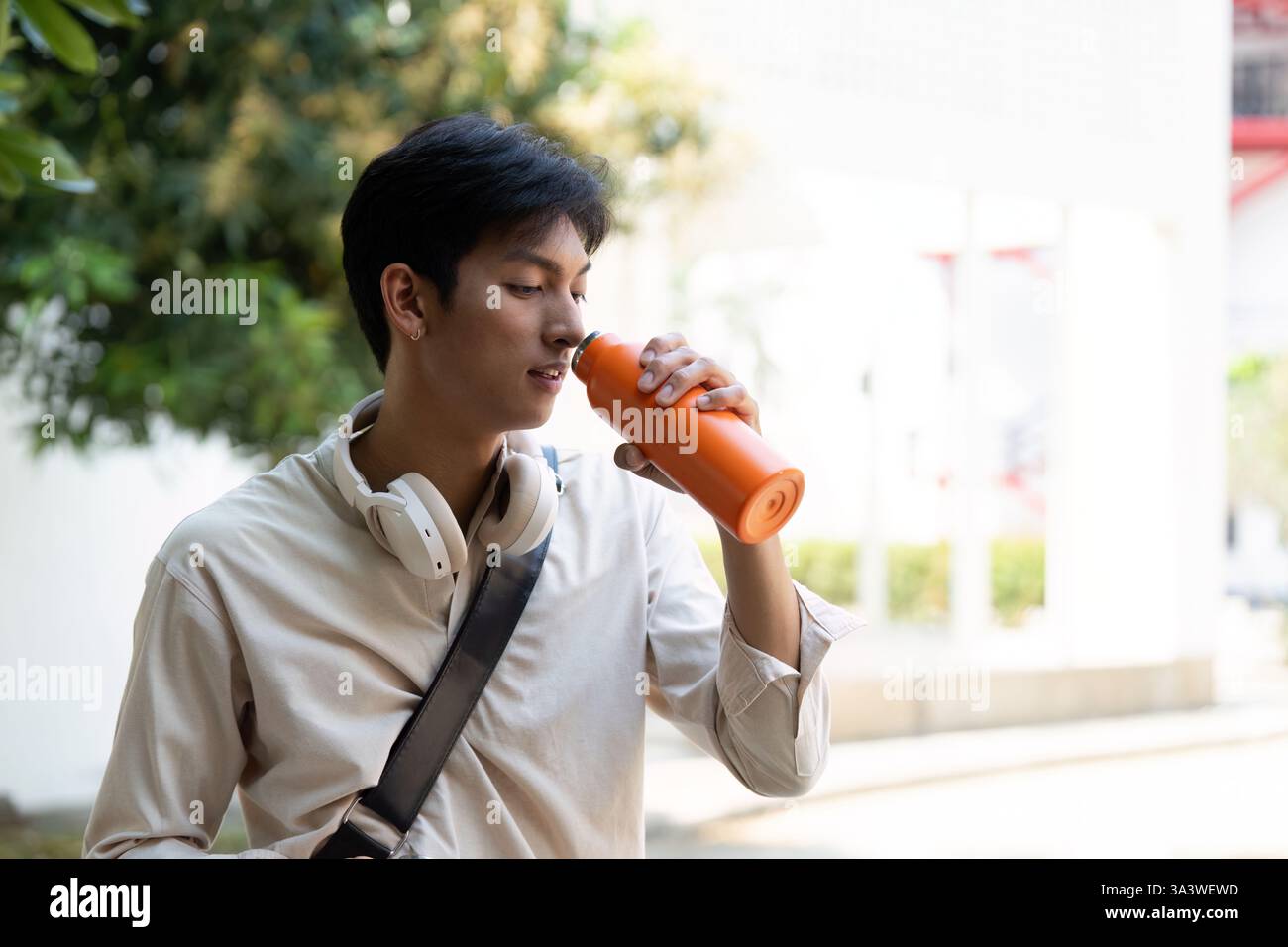 Nachhaltigkeit und Erfrischung. Ein junger Mann trinkt aus seiner wiederverwendbaren Wasserflasche, während er Outdoor-Aktivitäten genießt. Stockfoto