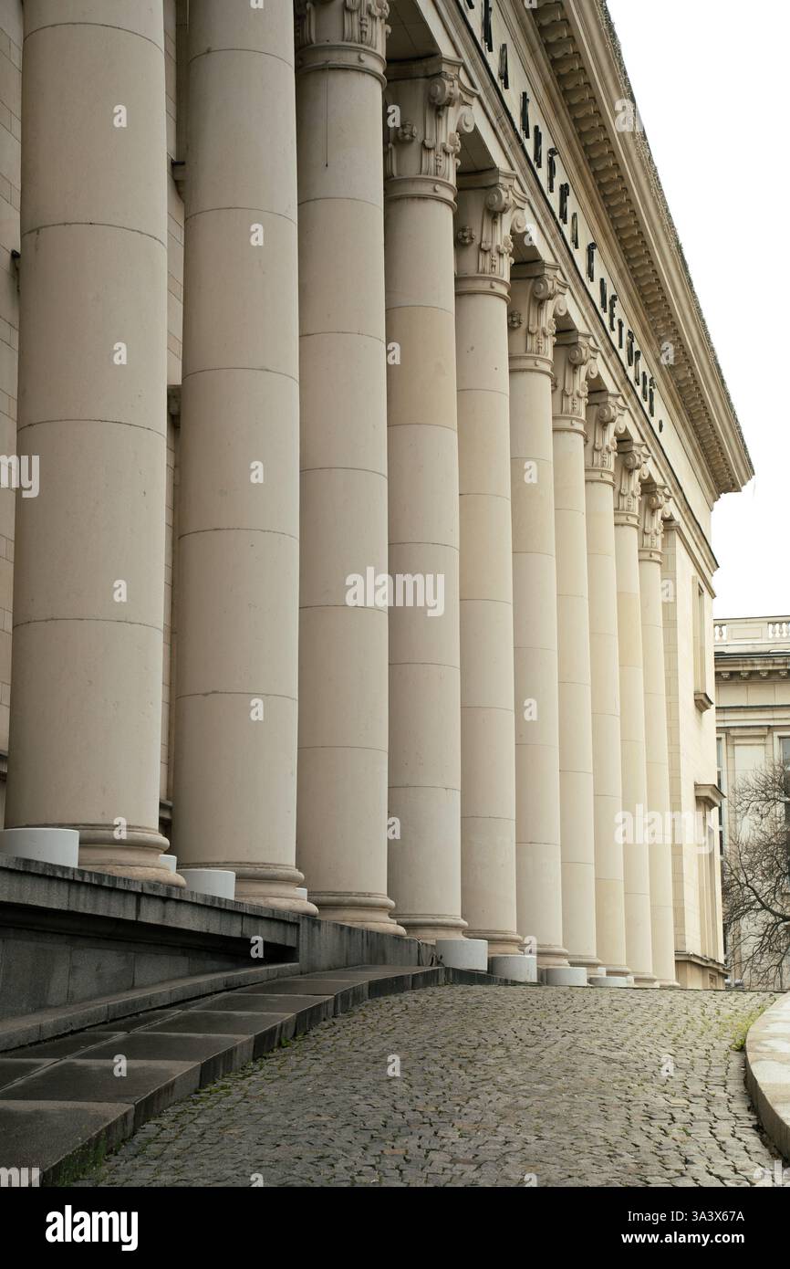 Neoklassizistische architektonische Säulen mit Kopfsteinpflasterweg, perspektivisch erfasst, Teil eines historischen institutionellen Gebäudes in Sofia, Bulgarien. Stockfoto
