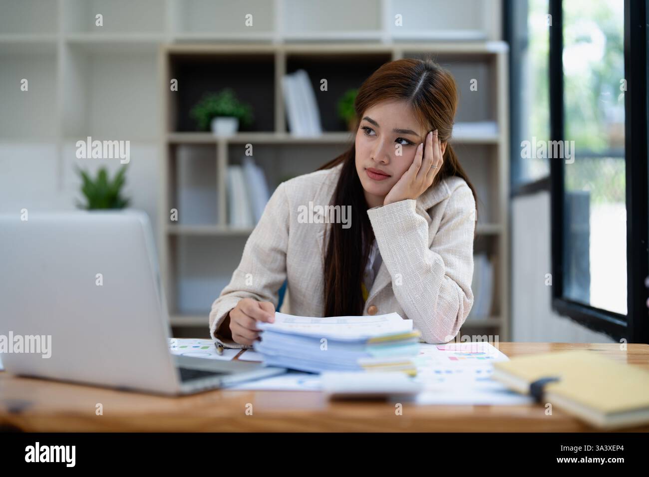 Gestresste junge Geschäftsfrau, die von Papierkram mit Finanzen, Marktdiagrammen und Dokumenten im Büro überwältigt wird. Stockfoto