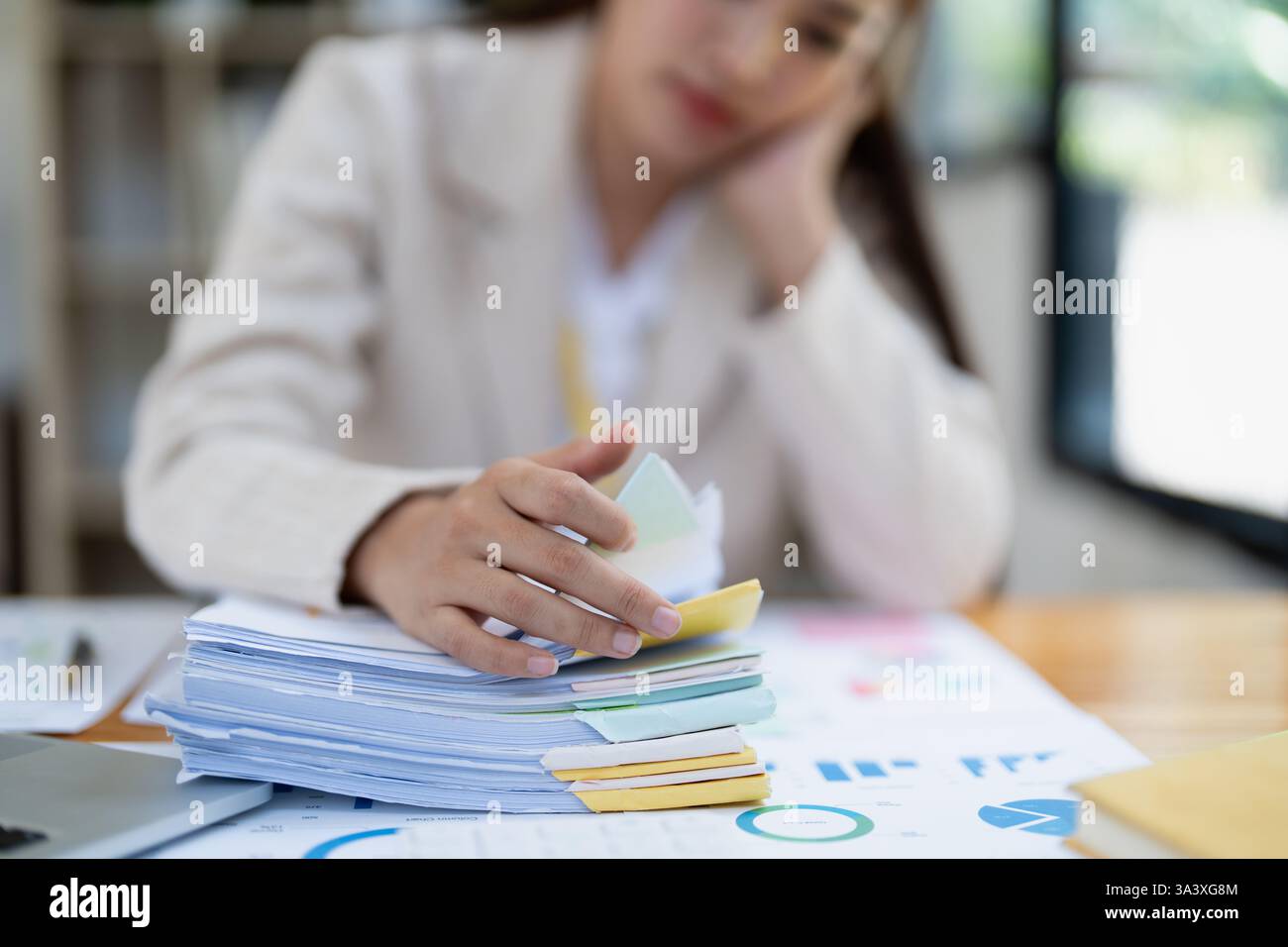 Gestresste junge Geschäftsfrau, die von Papierkram mit Finanzen, Marktdiagrammen und Dokumenten im Büro überwältigt wird. Stockfoto