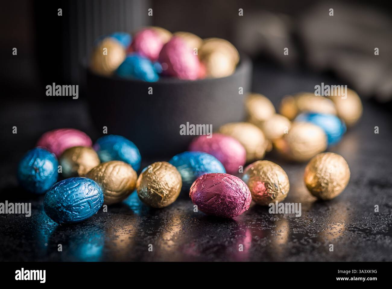 Schokoladen-ostereier in mehrfarbige Folie auf einem schwarzen Tisch. Stockfoto