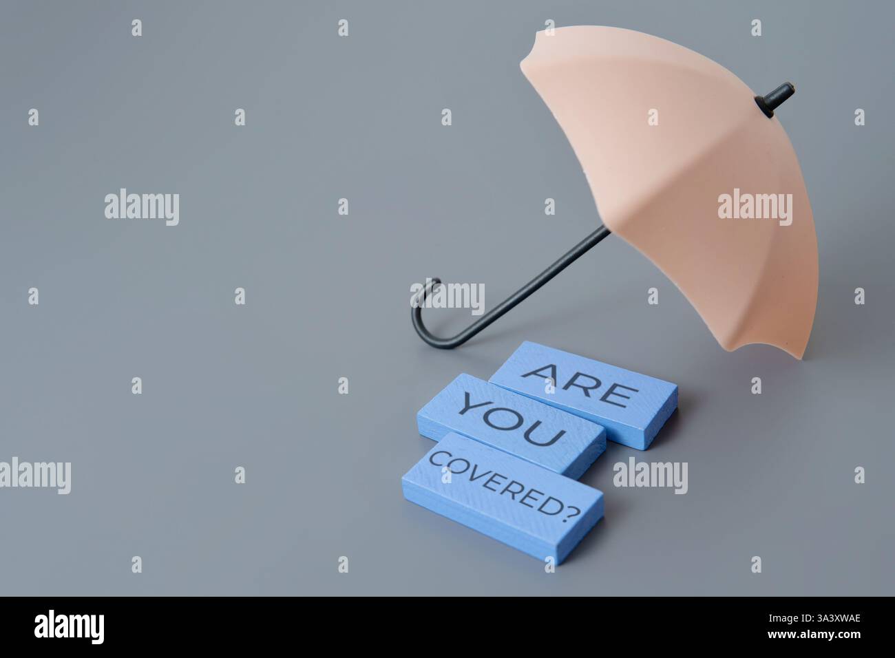 Ein kleiner Regenschirm mit den Worten „sind Sie bedeckt?“. Schutz, Versicherung, finanzielles Sicherheitskonzept. Stockfoto