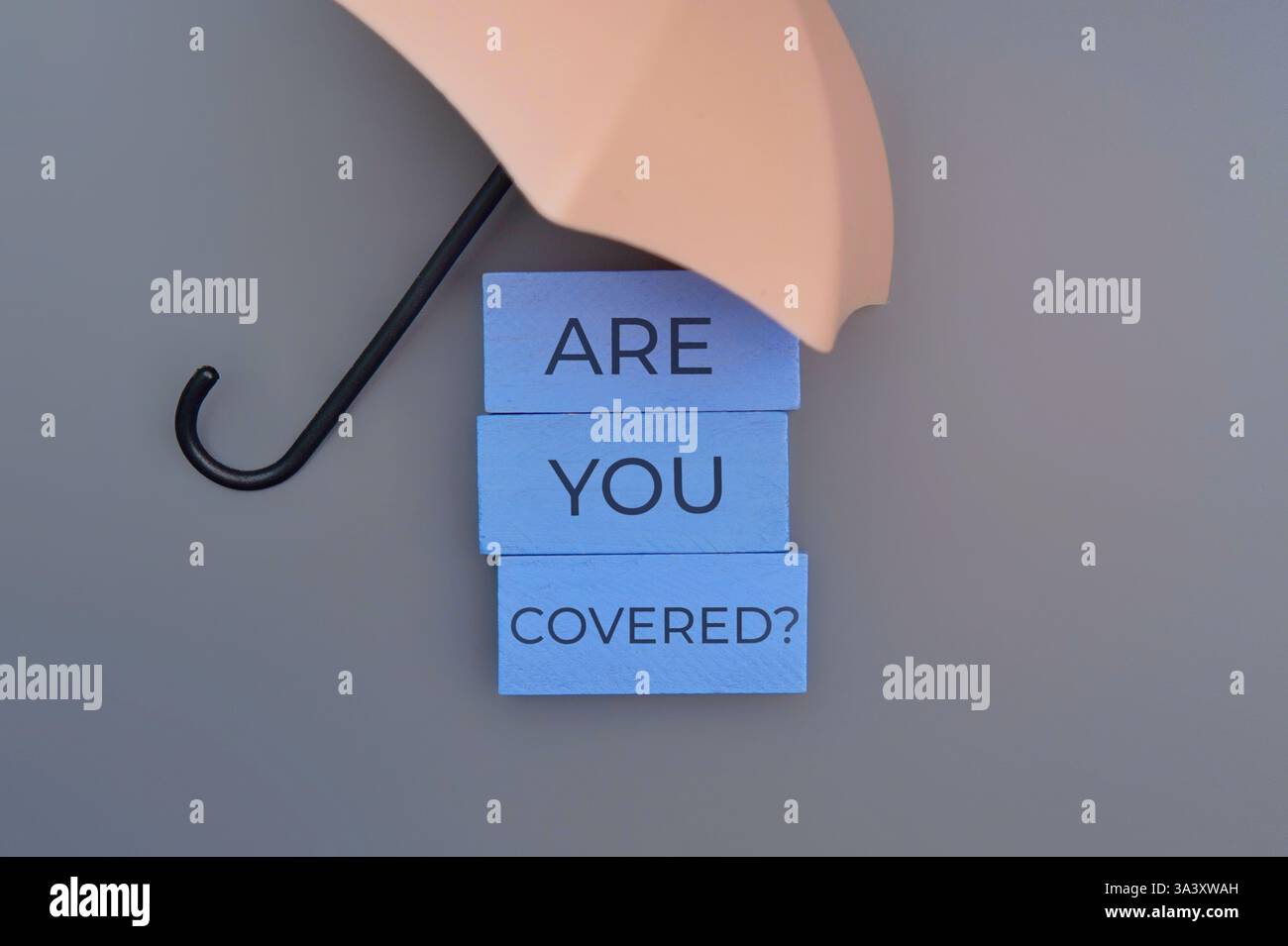 Ein kleiner Regenschirm mit den Worten „sind Sie bedeckt?“. Schutz, Versicherung, finanzielles Sicherheitskonzept. Stockfoto
