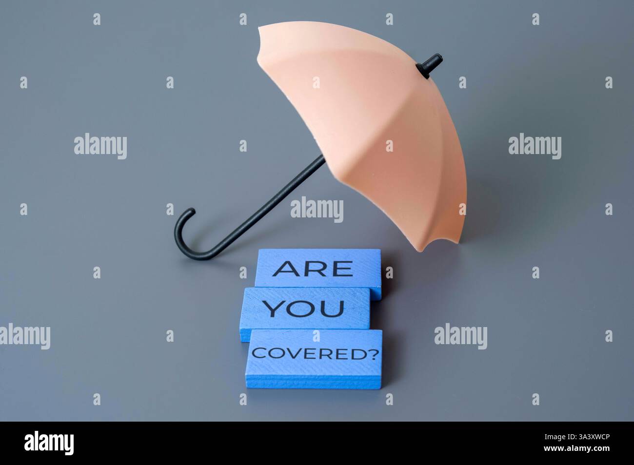Ein kleiner Regenschirm mit den Worten „sind Sie bedeckt?“. Schutz, Versicherung, finanzielles Sicherheitskonzept. Stockfoto