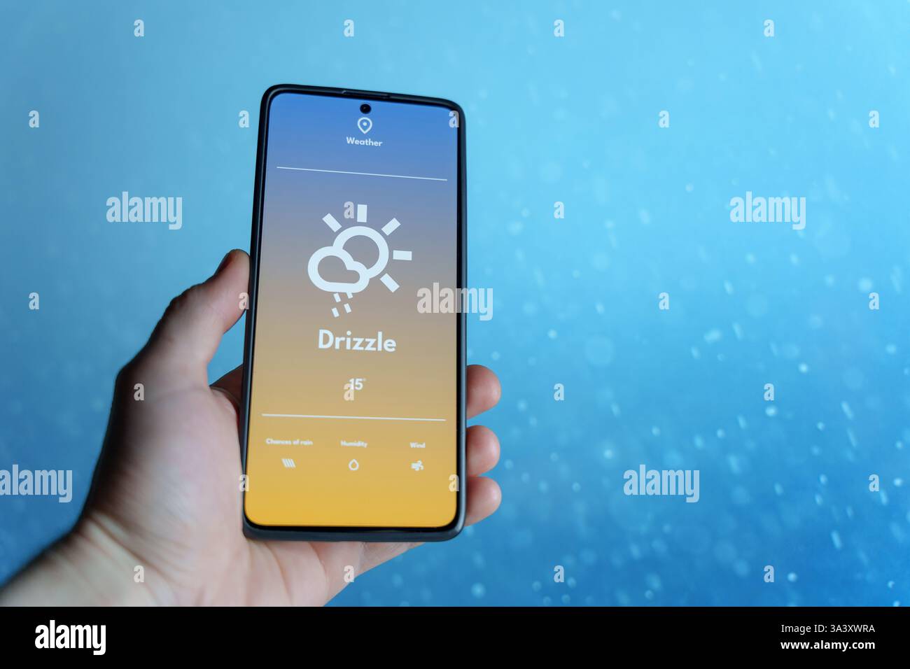 Hand hält ein Smartphone, das eine Wetter-App mit Nieselvorhersage anzeigt. Regentropfen fallen in den verschwommenen Hintergrund. Wettertechnologie und Wettervorhersage Stockfoto