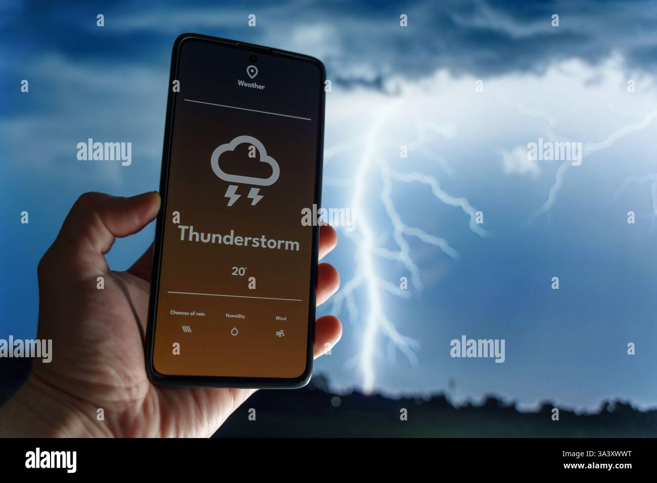 Hand hält ein Smartphone, das eine Wetter-App mit Gewittervorhersage anzeigt. Ein Blitz schlägt in den unscharfen Hintergrund. Extremes Wetter und tec Stockfoto