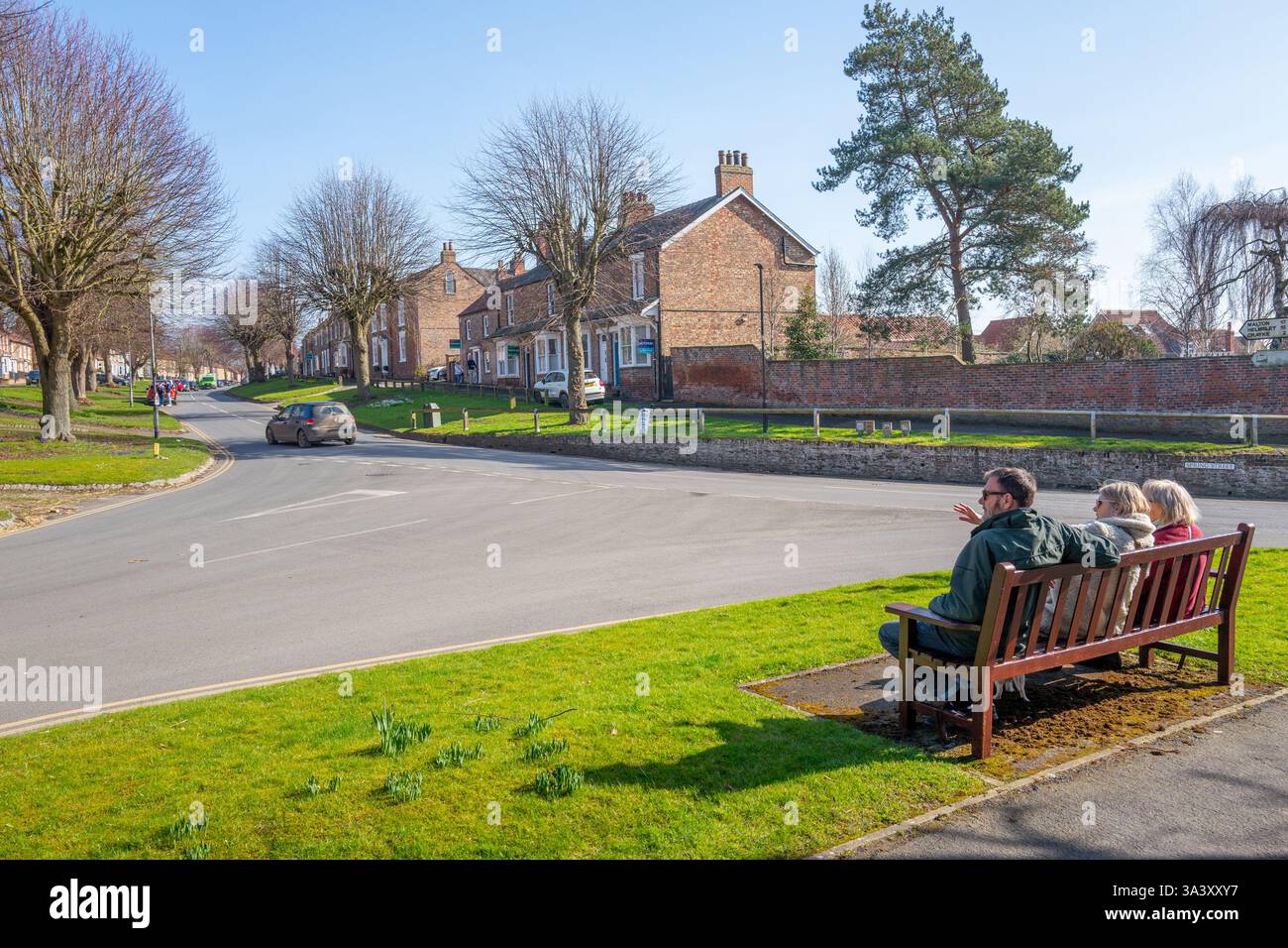 Drei Erwachsene saßen auf einer Holzbank an der Ecke von Church Hill und Spring Street in der Marktstadt Easingwold, North Yorkshire. Stockfoto