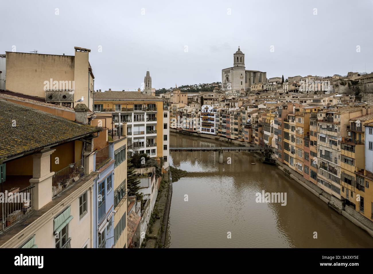Girona Stadt, Blick über den Onyar Fluss mit den hängenden Häusern über den Ufern und der Kathedrale im Hintergrund, an einem kalten, bewölkten Wintertag. Stockfoto