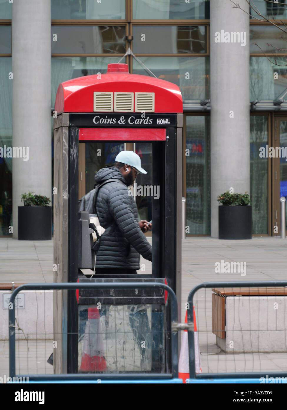 Mann eingerahmt von Telefonzelle mit fehlenden Fenstern, während er am Handy vorbeiläuft, Bishopsgate, London, Großbritannien Stockfoto