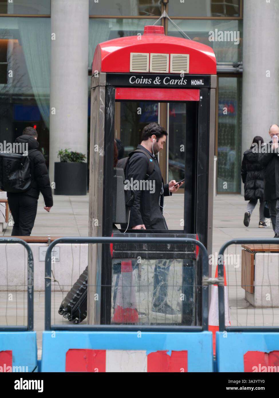 Mann eingerahmt von Telefonzelle mit fehlenden Fenstern, während er am Handy vorbeiläuft, Bishopsgate, London, Großbritannien Stockfoto
