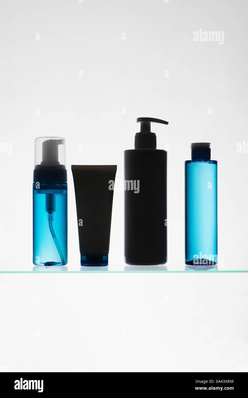 Сosmetic Produkte im Schatten auf einem Glasregal auf weißem Hintergrund. Mockup von Hautpflege- und Badeprodukten auf einem Glasregal. Spender und Röhrchen Stockfoto