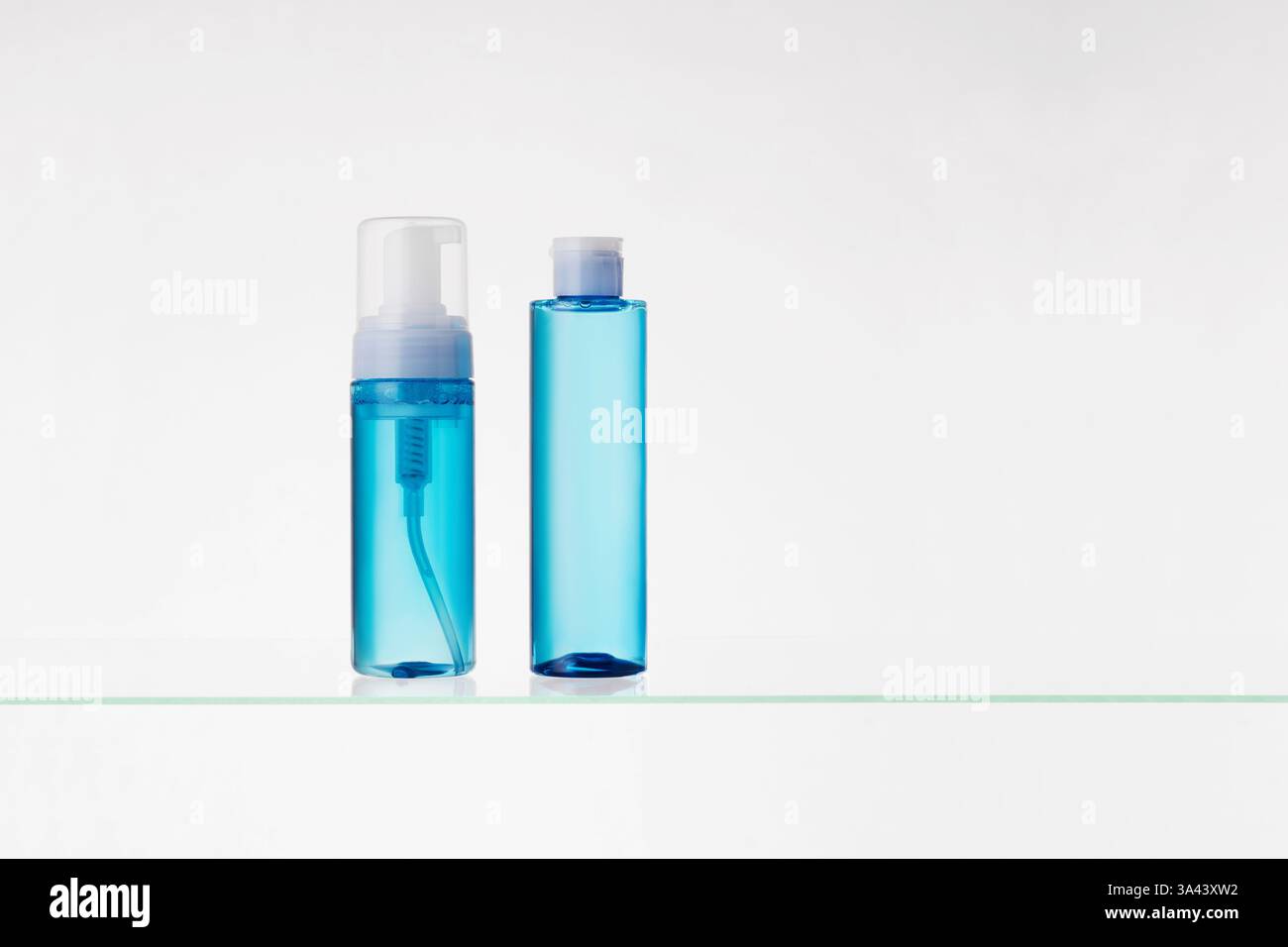 Blaue transparente Flaschen mit kosmetischen Produkten auf einem Glasregal auf weißem Hintergrund. Mockup von Hautpflege- und Badeprodukten auf einem Glasregal Stockfoto