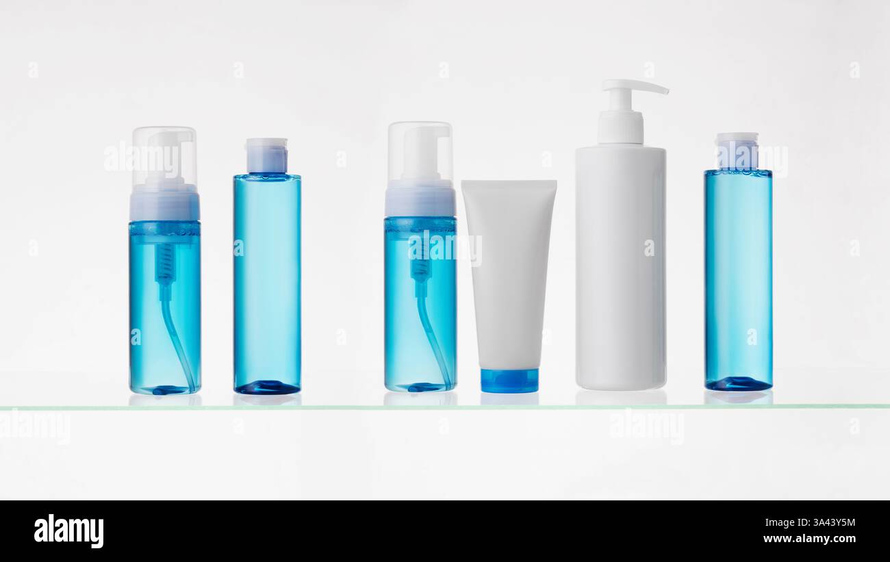 Verschiedene kosmetische Produkte auf einem Glasregal auf weißem Hintergrund. Mockup von Hautpflege- und Badeprodukten auf einem Glasregal. Spender und Röhrchen Stockfoto