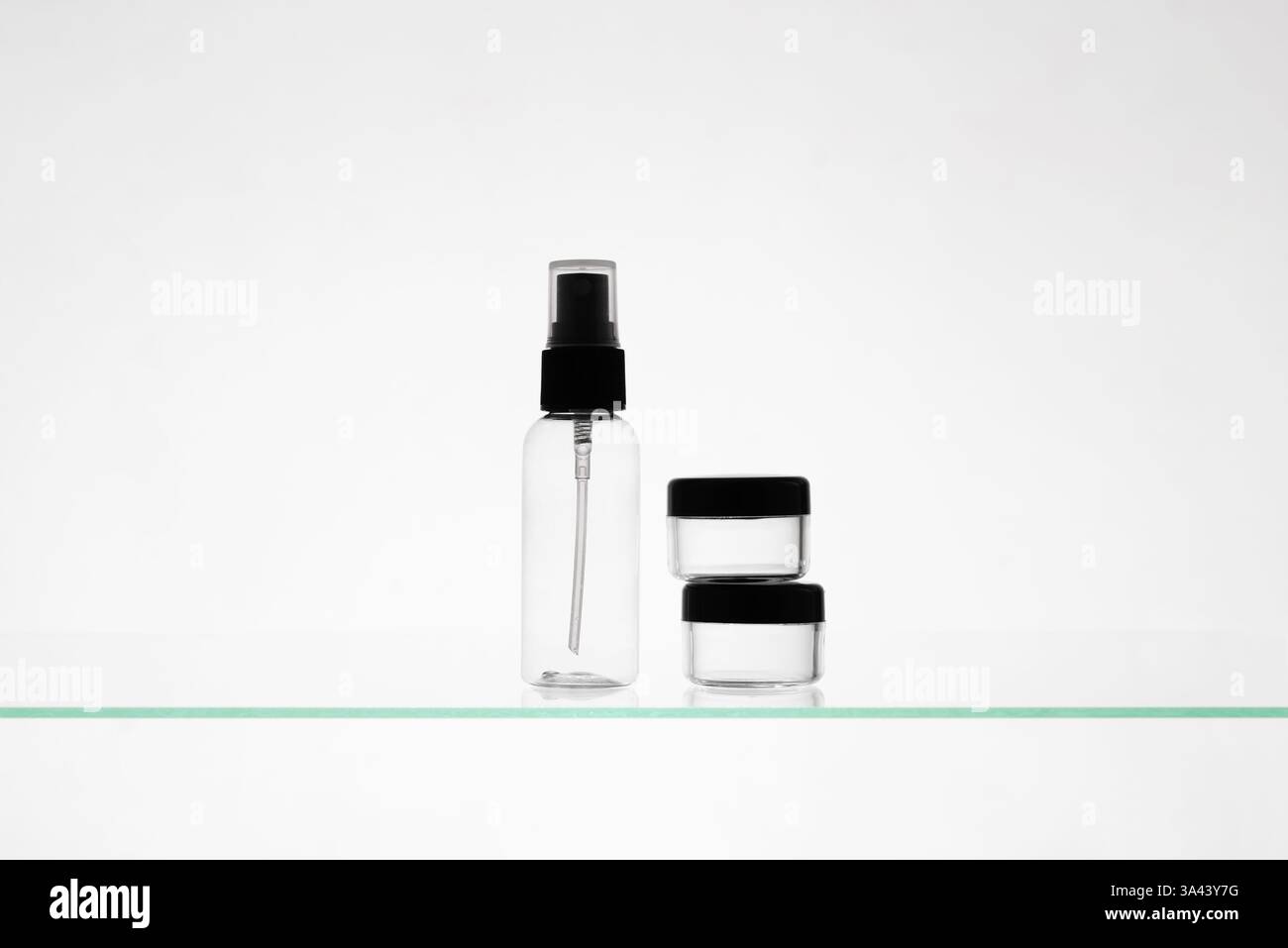 Leere Kosmetikprodukte auf einem Glasregal. Transparente Mockup-Flaschen in verschiedenen Größen für Werbung auf weißem Hintergrund Stockfoto
