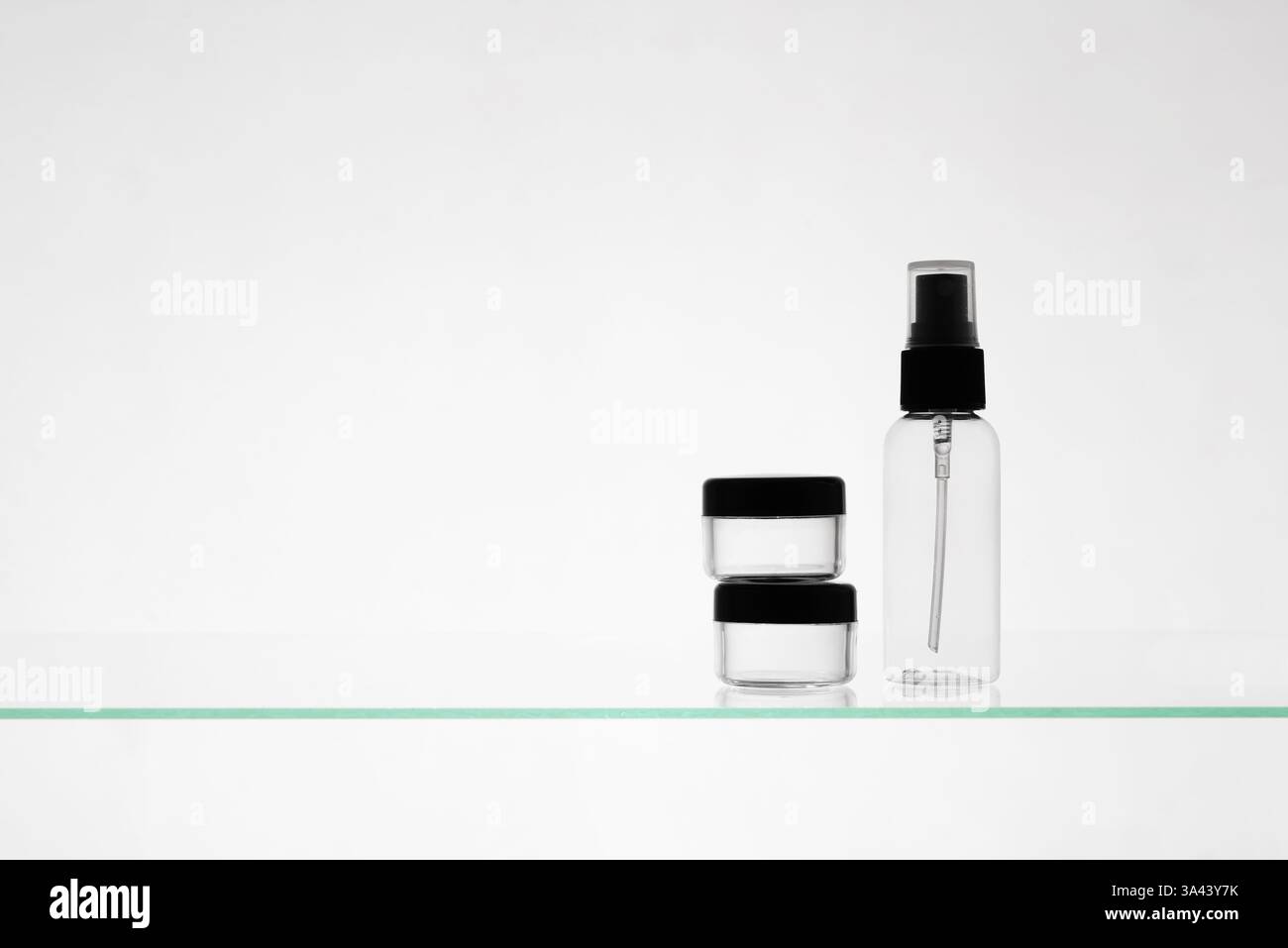 Leere Kosmetikprodukte auf einem Glasregal. Transparente Mockup-Flaschen in verschiedenen Größen für Werbung auf weißem Hintergrund Stockfoto