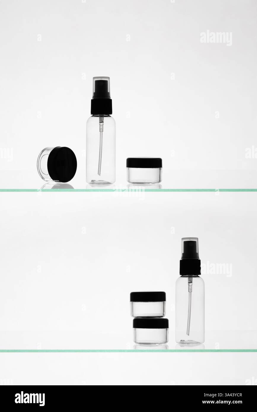 Leere Kosmetikprodukte auf einem Glasregal. Transparente Mockup-Flaschen in verschiedenen Größen für Werbung auf weißem Hintergrund Stockfoto