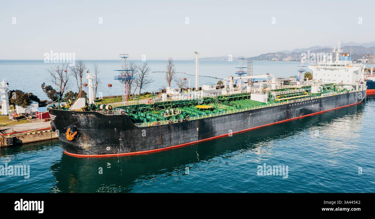 Öltanker, der am Industriehafen mit Rohrleitungen und Ladeinfrastruktur angedockt ist. Großes Frachtschiff für den Transport von flüssigem Kraftstoff, Petrochemikalien und Rohöl. Küstenschifffahrt. Stockfoto