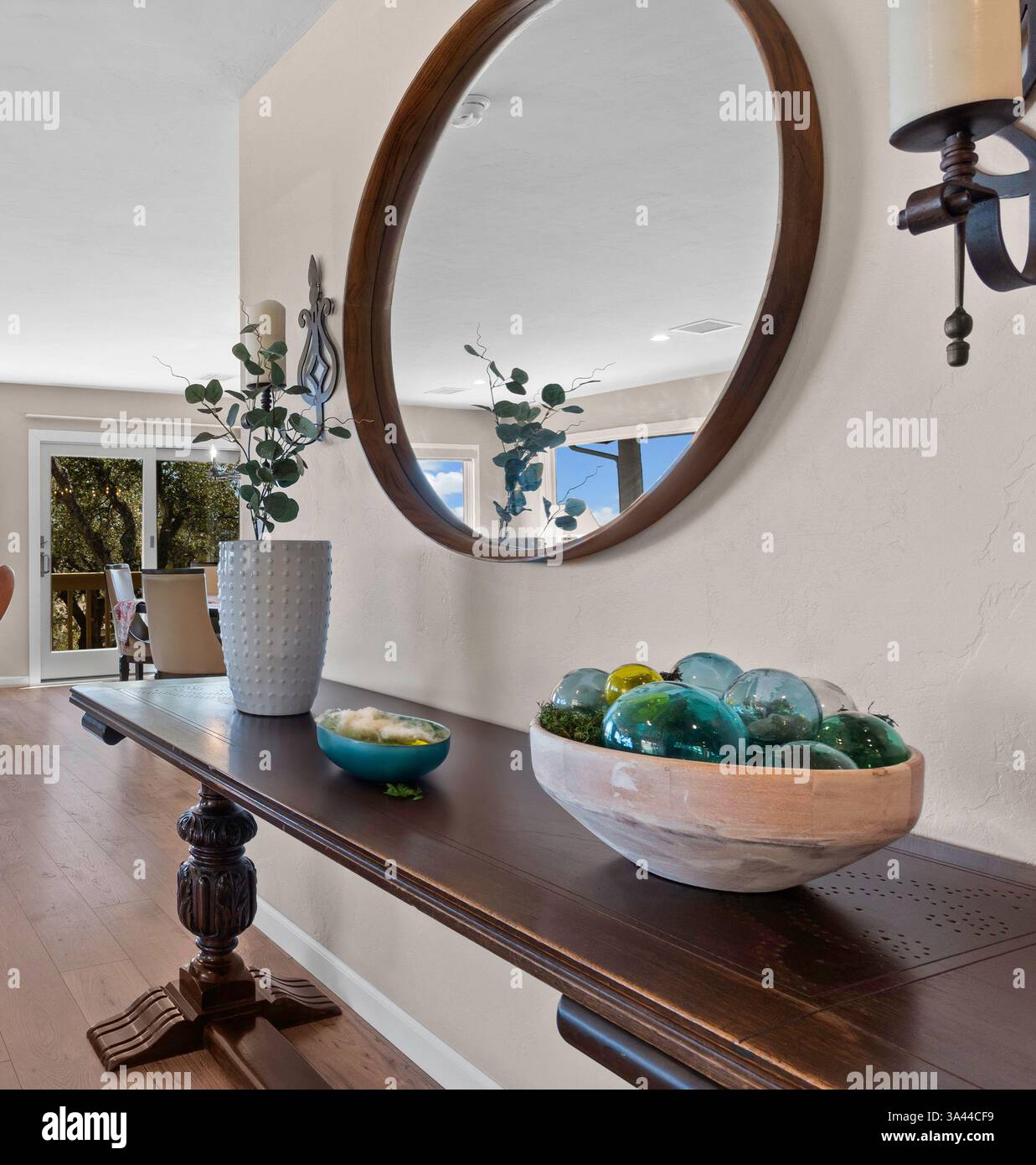Auf einem wunderschön angeordneten Tisch befindet sich neben einem eleganten Spiegel eine fesselnde Schüssel, gefüllt mit einer Auswahl an bunten Glasperlen Stockfoto