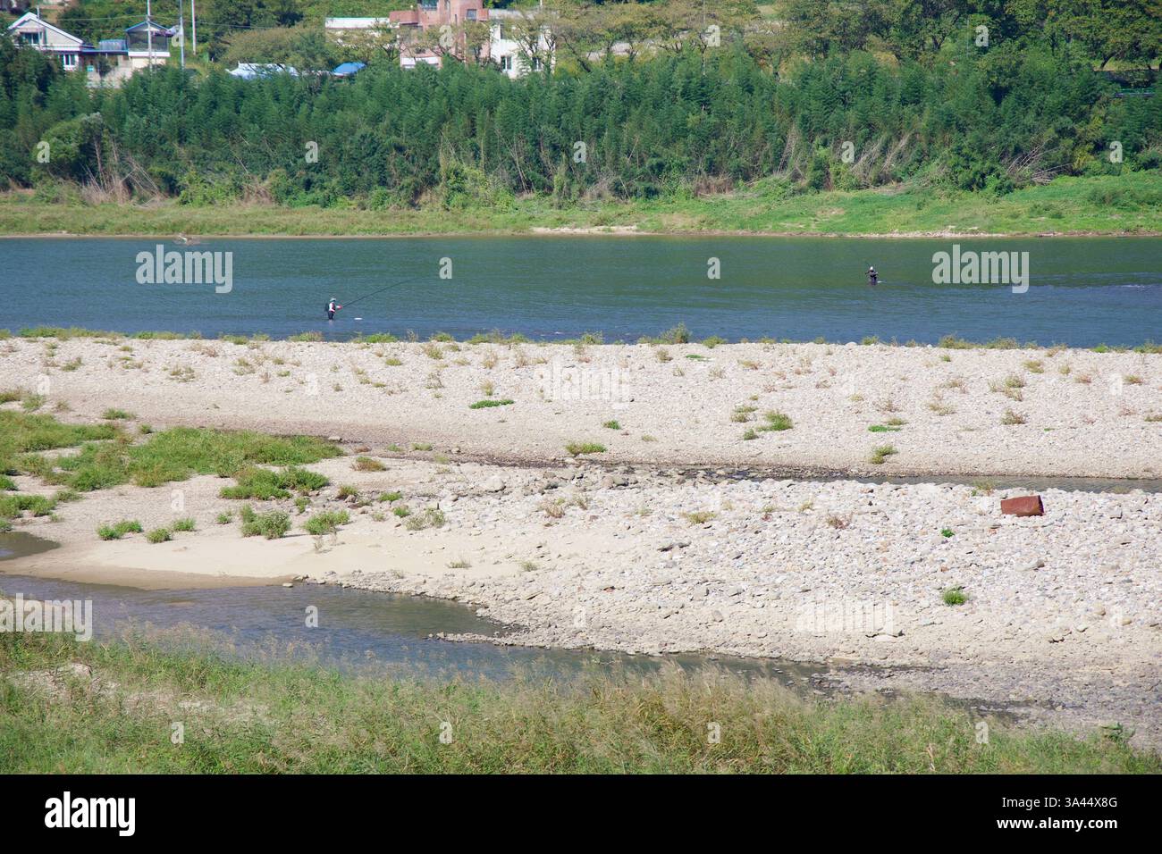Gwangyang City, Südkorea - 3. Oktober 2021: Zwei Fischer waten im Seomjingang River und werfen ihre Linien in das fließende Wasser, umgeben von Stockfoto