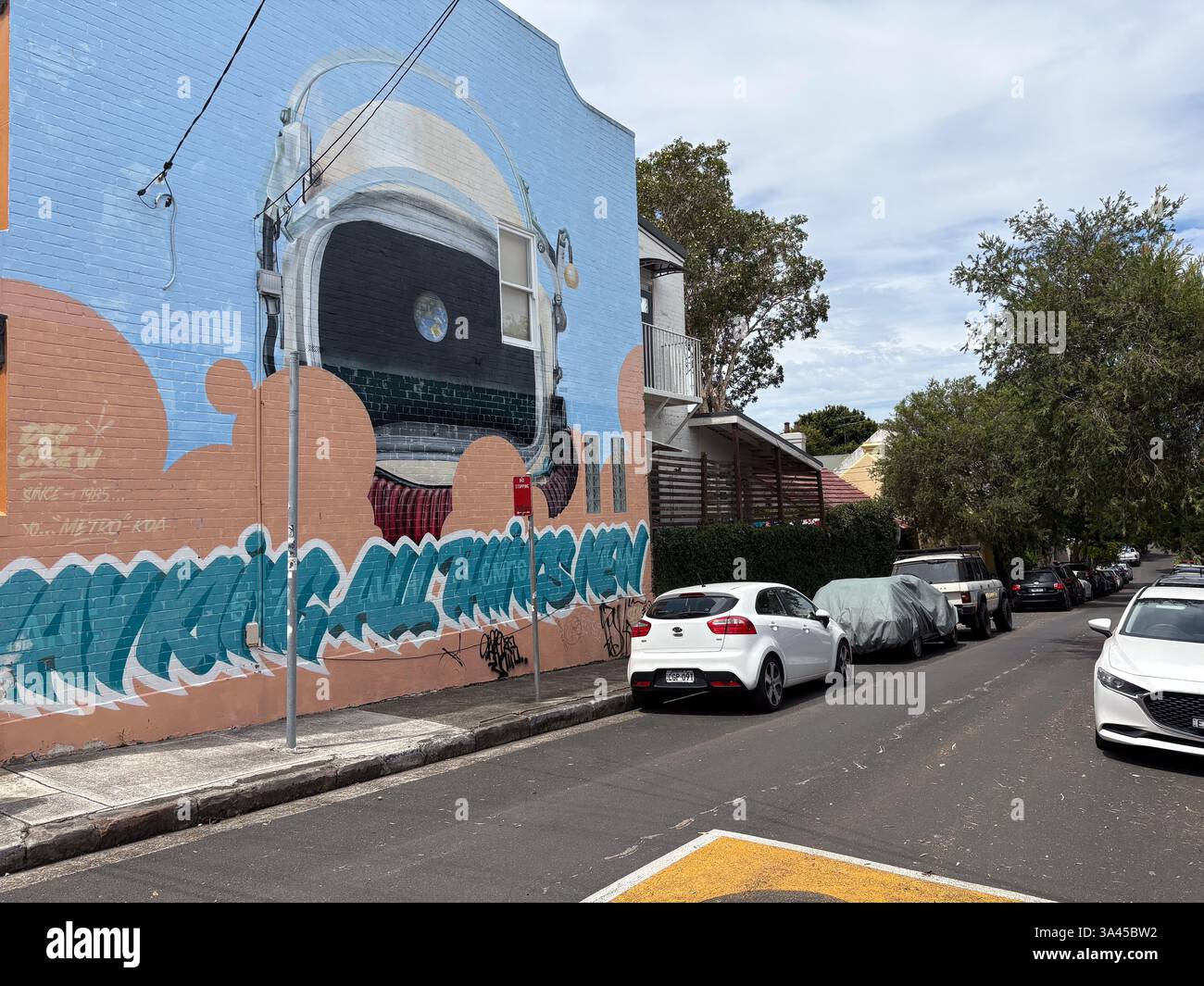 Graffiti-Wandgemälde eines Astronautenhelms in einem Gebäude in Sydney, entlang einer Wohnstraße mit geparkten Autos zu sehen. Stockfoto