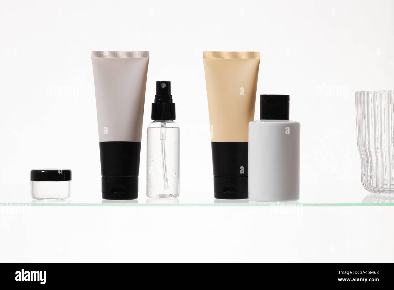 Verschiedene kosmetische Produkte auf einem Glasregal auf weißem Hintergrund. Mockup von Hautpflege- und Badeprodukten auf einem Glasregal. Spender und Röhrchen Stockfoto