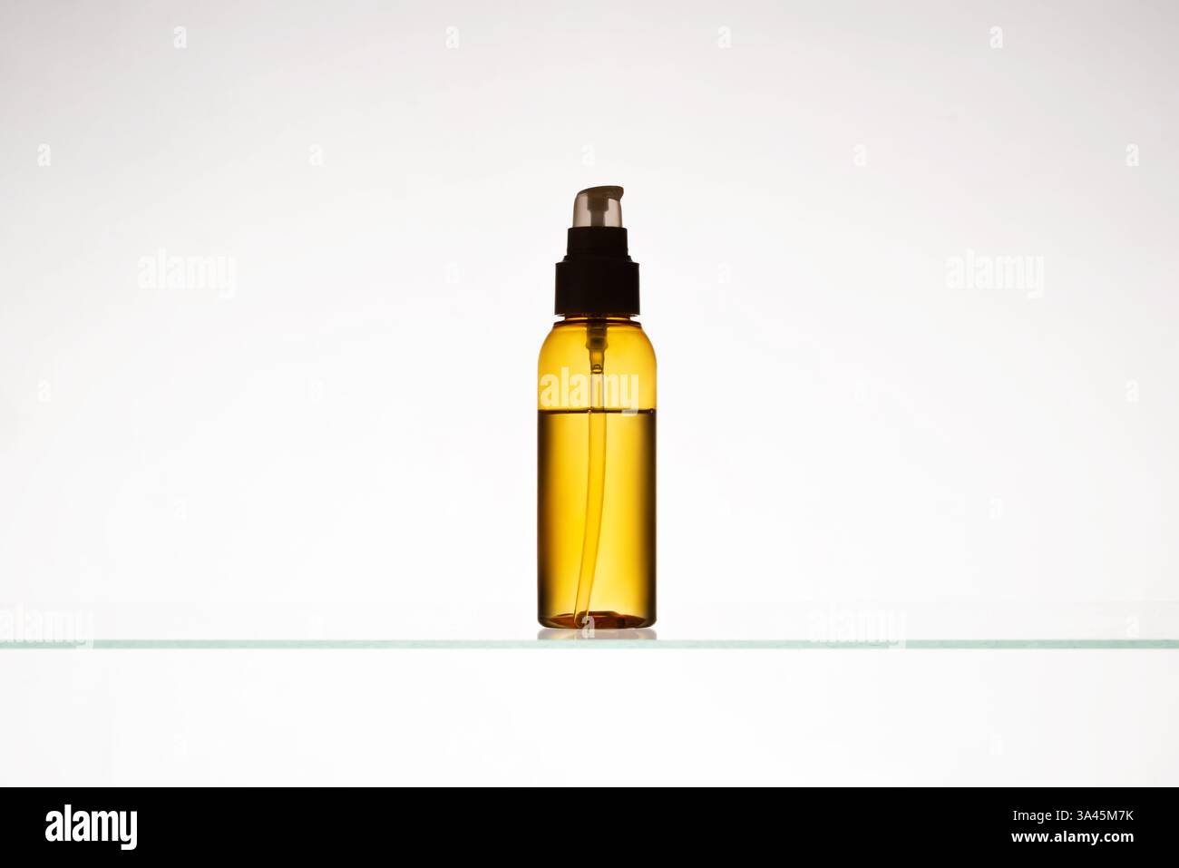 Ölflasche oder gelbe Hautpflegeessenz auf einem Glasregal. Transparente Flasche mit einem kosmetischen Produkt auf weißem Hintergrund. Minimales Schönheitsprodukt Stockfoto