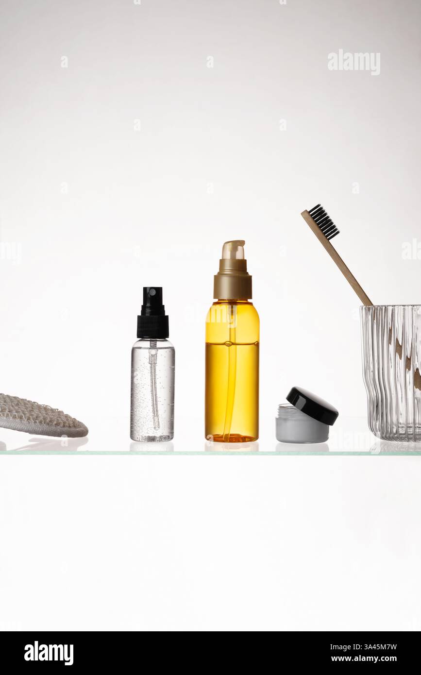 Verschiedene kosmetische Produkte auf einem Glasregal auf weißem Hintergrund. Mockup von Hautpflege- und Badeprodukten auf einem Glasregal. Spender und Röhrchen Stockfoto