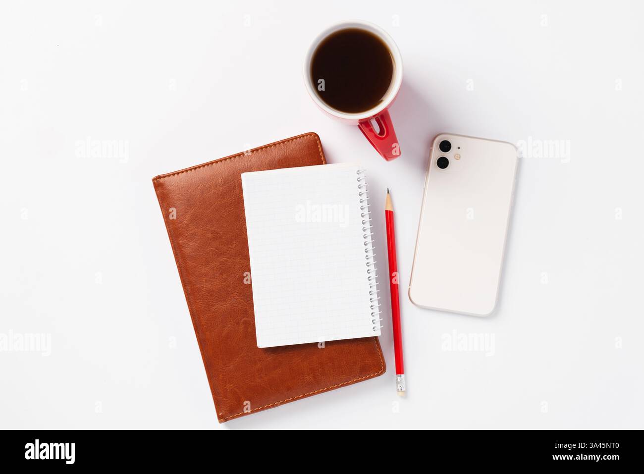 Braunes Notizbuch, roter Bleistift, weißes Smartphone und rote Tasse mit Kaffee auf weißem Hintergrund. Morgendämmerpläne für den Tag, Arbeitsplatz Stockfoto