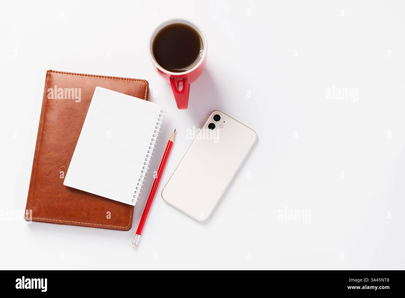 Braunes Notizbuch, roter Bleistift, weißes Smartphone und rote Tasse mit Kaffee auf weißem Hintergrund. Morgendämmerpläne für den Tag, Arbeitsplatz Stockfoto