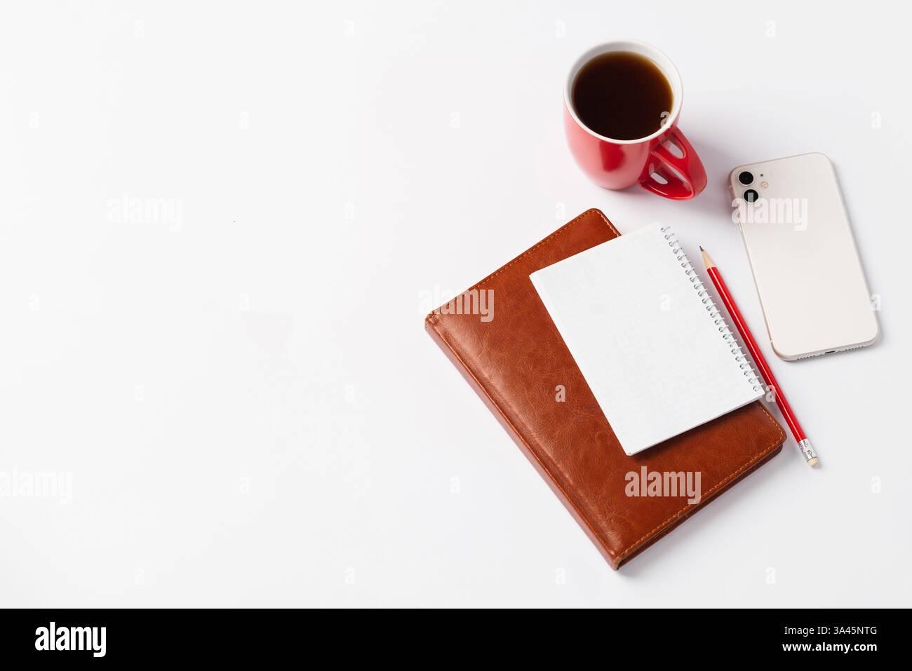 Braunes Notizbuch, roter Bleistift, weißes Smartphone und rote Tasse mit Kaffee auf weißem Hintergrund. Morgendämmerpläne für den Tag, Arbeitsplatz Stockfoto