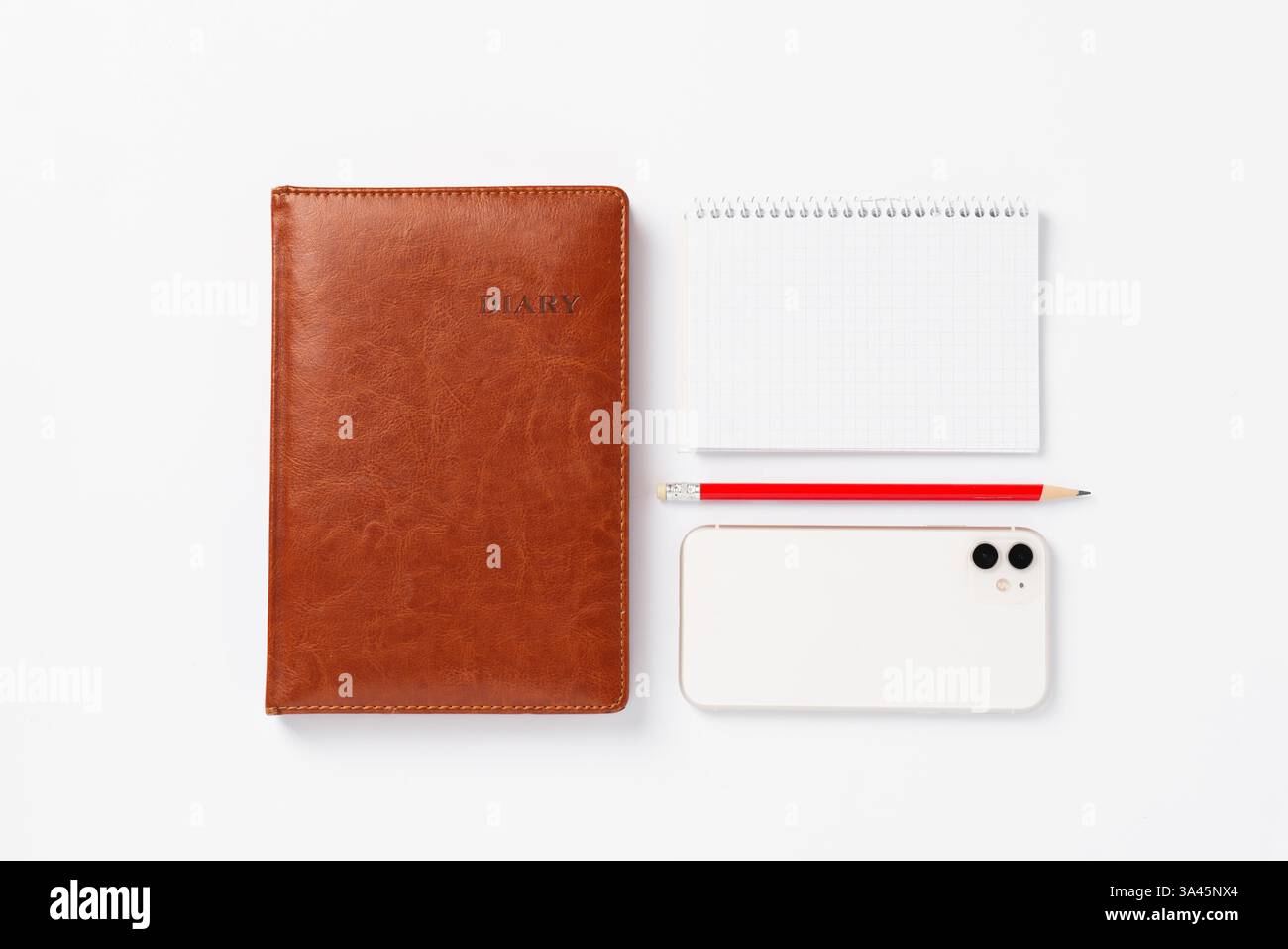 Braunes Notizbuch, roter Bleistift, weißes Smartphone und rote Tasse mit Kaffee auf weißem Hintergrund. Morgendämmerpläne für den Tag, Arbeitsplatz Stockfoto