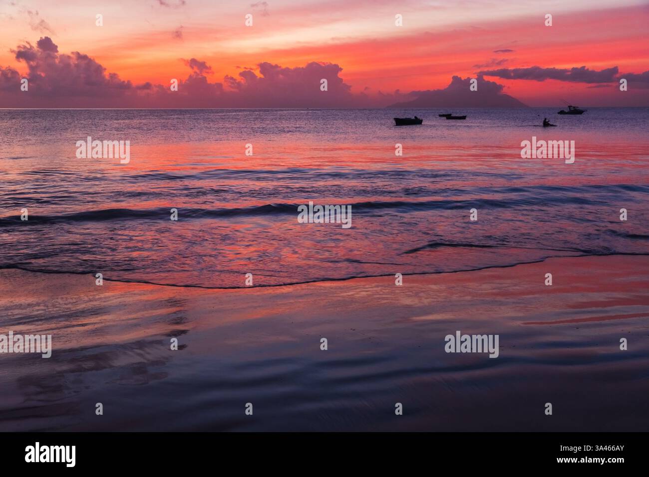 Wunderschöner Meerblick bei Sonnenuntergang mit lebhaften Farben, ruhigen Wellen und kleinen Booten auf ruhigem Wasser, die Ruhe und Ruhe wecken. Mahe Island beac Stockfoto