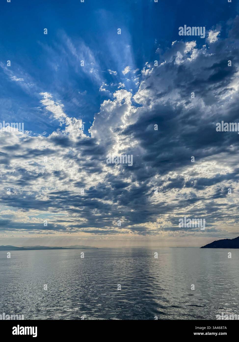 Sonnenlicht strömt durch einen strukturierten Himmel über einem weiten Ozean und schafft eine dynamische Wolkenlandschaft. Der Horizont dehnt sich mit weicher, plätschernder Wasserseele Stockfoto