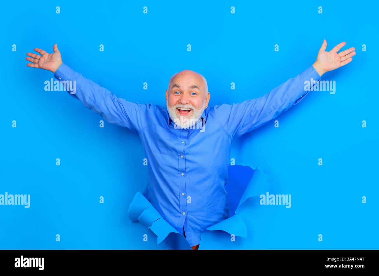 Glücklicher alter bärtiger Mann mit blauen Kontaktlinsen, der durch ein Loch im Papier schaut. Lächelnder Seniorenmann in stilvollem Hemd erhob die Hände. Gutaussehender männlicher Blick Stockfoto