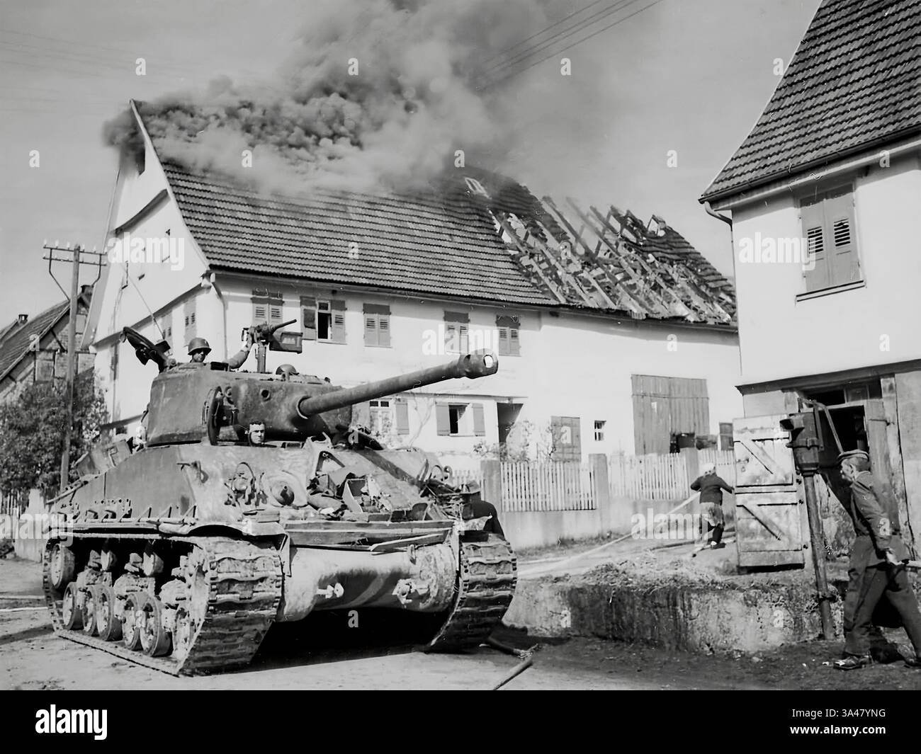 Die letzten Tage des Zweiten Weltkriegs (1945) und amerikanische Truppen der 10. Panzerdivision und eines Sherman-Panzers ziehen durch eine brennende Stadt in Deutschland vor Stockfoto