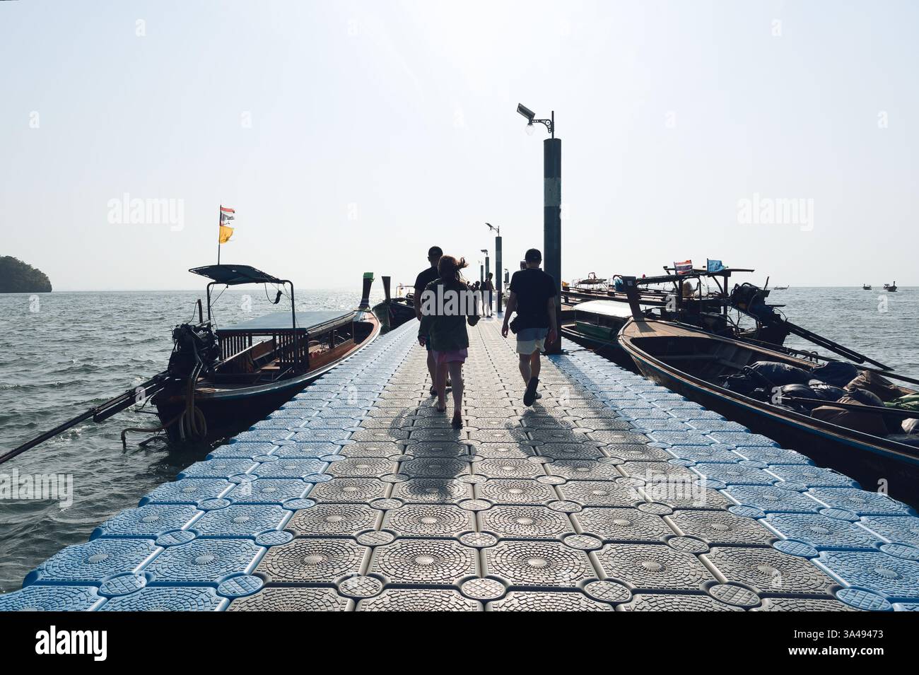 Touristen spazieren entlang eines schwimmenden Piers, flankiert von Langboot-Booten in East Railay. Stockfoto